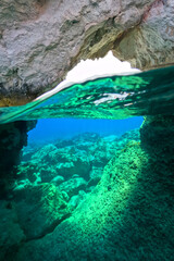 Underwater split photo of small cove and arch rock formations near  famous for colourful boat houses area of Karas, Kimolos island, Cyclades, Greece