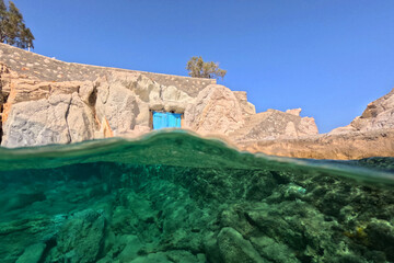 Underwater split photo of small cove and arch rock formations near  famous for colourful boat houses area of Karas, Kimolos island, Cyclades, Greece