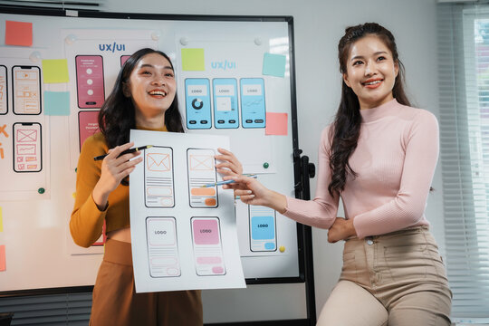Two asian women web designers discussing over mobile application wireframe design prototypes in a meeting room