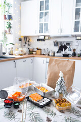 Delivery of sushi and rolls in food containers on the table in the festive interior of the kitchen of the house with a white Christmas tree for Christmas and New year. Food delivery for the holidays