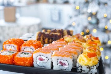 Delivery of sushi and rolls set is hold in hand in the festive interior of house with a white Christmas tree for Christmas and New year. Food delivery for the holidays