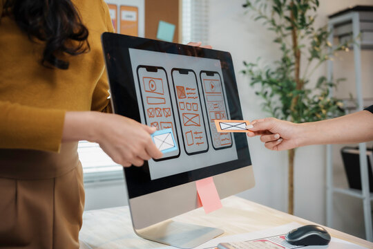 Two female user experience designers are comparing paper prototypes of a mobile application interface