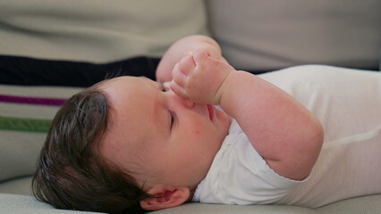 Close-up of baby lying on a couch, gazing attentively while relaxing indoors in a comfortable and...