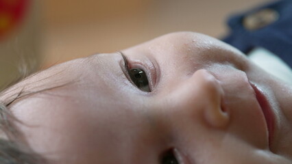 Naklejka premium Close-up of baby lying on its side, focusing on the eye and soft skin textures. The baby looks calm and curious, with a soft focus on the face in natural lighting