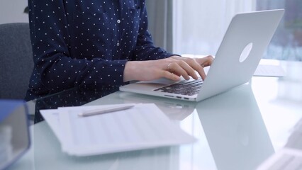 A female accountant or businesswoman with blue dotted blousy is typing on laptop computer on glass...