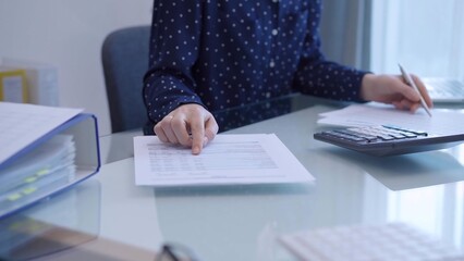 A female accountant with blue dotted blousy is using a laptop computer and calculator to calculate...