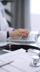 Stethoscope with a medication history record form are on the glass table. Doctor woman is working with laptop computer on the background. Medicine concept