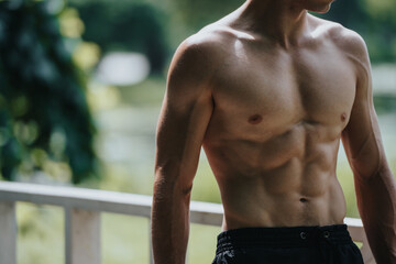 Athletic shirtless man showcasing his muscular abs during an outdoor workout, highlighting fitness, strength, and a healthy lifestyle.