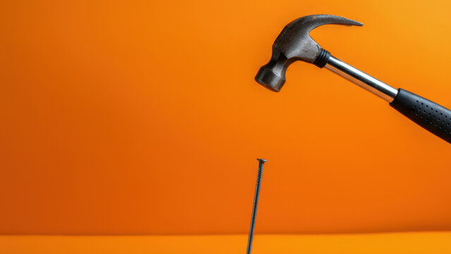 Hammer about to strike nail against orange background