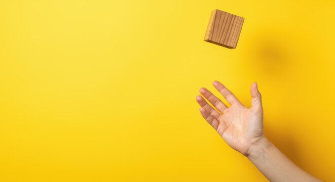 Hand tossing wooden block against bright yellow background