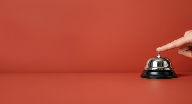 Hand pressing silver service bell on red surface