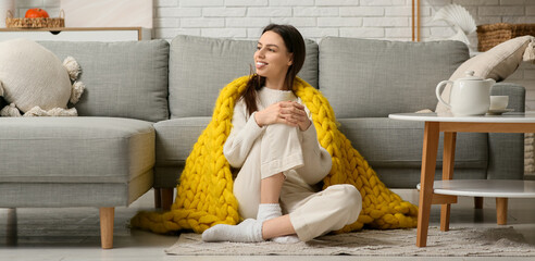 Beautiful young woman with warm yellow plaid sitting on floor in living room
