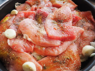 Tender cuts of meat are spiced and arranged for cooking, surrounded by garlic and herbs, creating a savory dish steeped in rich flavors and aromas. Raw meat is soaked in beer for baking in the oven.