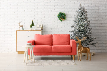 Beautiful Christmas tree with chest of drawers and comfortable sofa near white brick wall