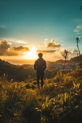 Fototapeta premium A person admiring a sunset over hills and a small town while walking on a grassy trail in the countryside during late afternoon