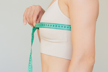 Close-up profile of young pretty Caucasian brunette woman in beige underwear measuring her chest...