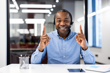 Smiling african american mature businessman using headset in office environment. Engaged in online...