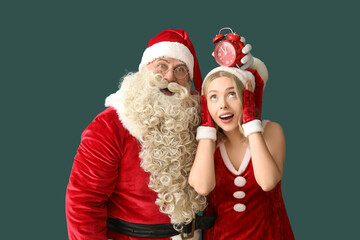 Santa Claus and beautiful woman with alarm clock on green background