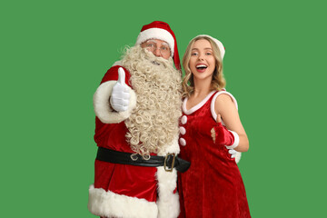Happy young woman with Santa Claus showing thumb-up on green background