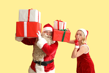 People dressed as Santa Claus with Christmas gifts showing silence gesture on yellow background