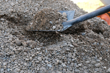 Shovel with sand and gravel mixture on background of pile, bulk building materials for preparation of concrete solution, DIY construction