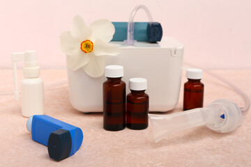 Modern nebulizer with inhalers, bottles and daffodil flower on pink grunge table