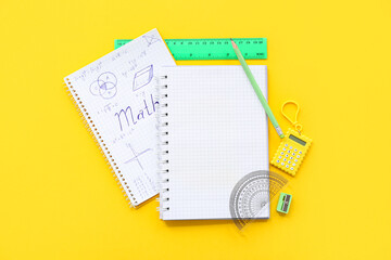 Notebooks with calculator and school stationery on yellow background
