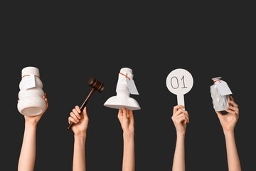 Female hands with auction paddle, gavel and antique items on dark background