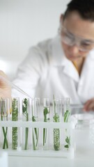 Woman scientist wearing a lab coat, is dripping liquid from a pipette into a test tube with a green...