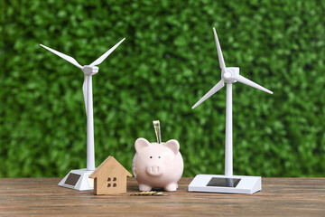 Wind turbine models with house figure and piggy bank on table outdoors. Green Energy concept
