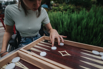 A boy with Down syndrome and a girl in a wheelchair engaged in a friendly game of backgammon, enjoying each other's company outdoors.