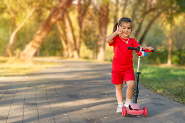 A little girl on a scooter in the park. The sun is shining brightly.
