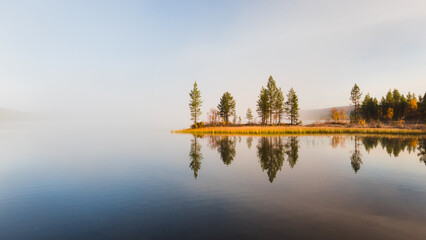 Calm water reflects trees during autumn morning in the Lapland arctic nature during ruska session evokes calm, peaceful and solitude, Finland