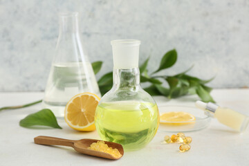 Bottle of oil, laboratory glassware with samples and ingredients for preparing natural cosmetics on white table near grunge wall
