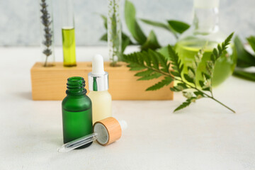 Bottles of oil, laboratory glassware with samples and ingredients for preparing natural cosmetics on white table near grunge wall