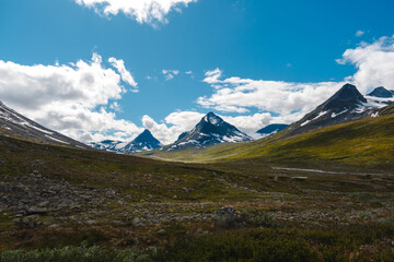 Scenic view when hiking to Visdalen valley with the nordic harsh tundra nature, white clouds over the snow covered mountains and steep summits during sunny day in Jotunheimen national park, Norway.