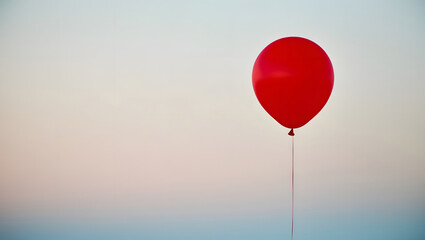 A bright red balloon floats freely amidst a calm pale blue sky, creating a sense of weightlessness and freedom, with space.
