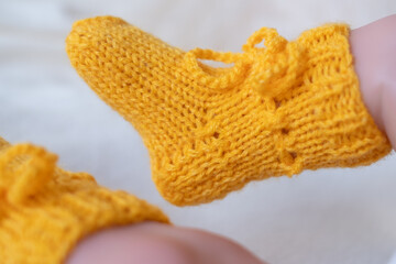 Soft yellow knitted booties for infants featuring delicate lacing and ribbed texture displayed on a baby\'s feet