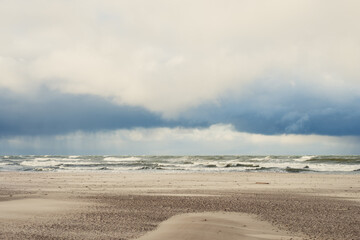 A tranquil beach under a dramatic sky with rolling waves, captured in an early afternoon setting near the ocean
