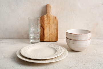 Clean plates, bowls, glasses and board on table against white grunge background