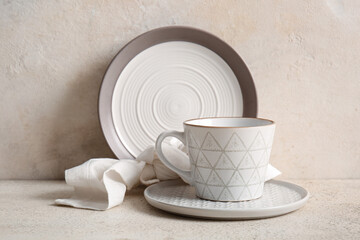 Clean plate, saucer, cup and napkin on table against white grunge background
