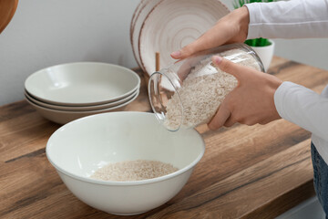 Woman pouring rice into bowl near table in kitchen, closeup