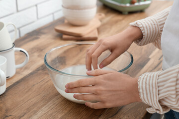 Woman rinsing rice in glass bowl near wooden table, closeup