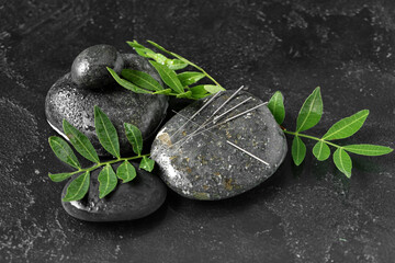 Acupuncture needles and spa stones on dark background