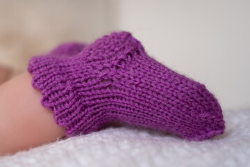 Cozy purple knitted baby booties resting on a soft white blanket in a warm indoor setting during daylight