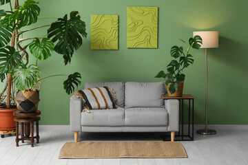 Monstera houseplants, glowing lamp, coffee table and sofa near green wall