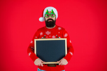 Santa Claus bearded man in hat and Christmas sweater hold Xmas advertisement for new 2024 year...
