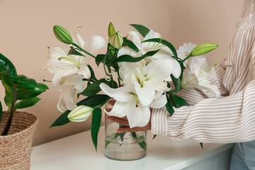 Beautiful young African-American woman with vase of white lily flowers bouquet at home, closeup