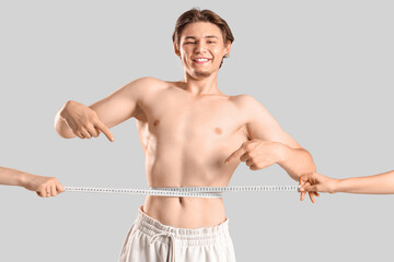 Fototapeta premium Female hands measuring young man's waist on light background. Weight loss concept