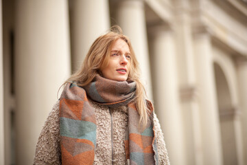 Woman in a cozy scarf walks near classical architecture on a sunny day